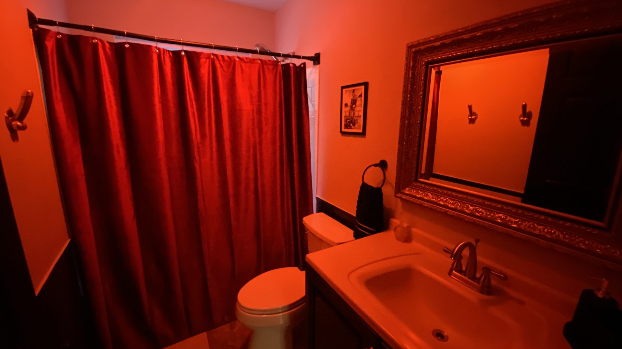 Bathroom with red curtain and framed mirror under red light