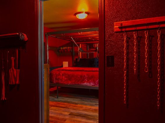 Floggers, paddles and chains on the wall, looking through to the Bondage Suite