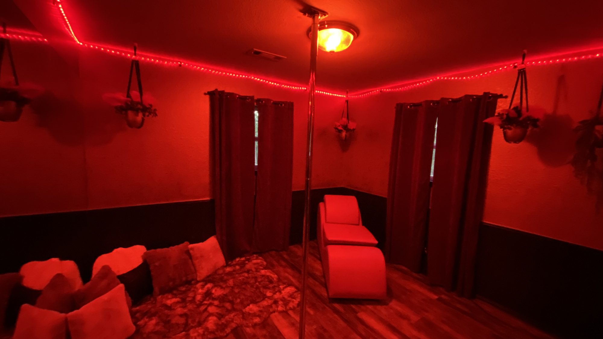 The Pole Lounge under red light with performance pole, chaise and floor pillows