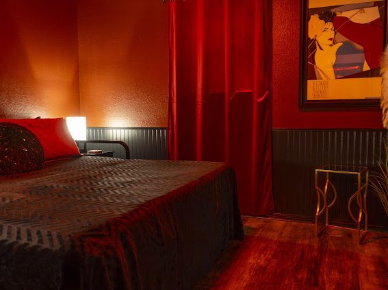 Bedroom with red velvet curtains, black wainscoting and fashion-illustration art